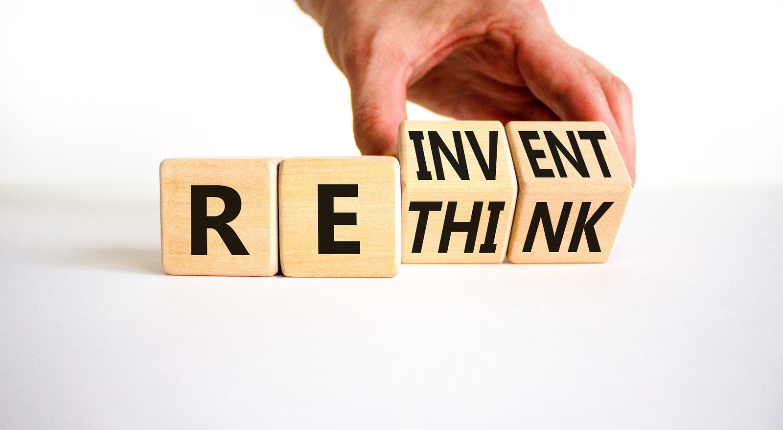 Wooden blocks spelling REINVENT, with a hand turning one block — a visual metaphor for business model reinvention.